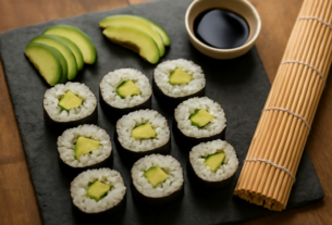 Sushi roll buatan rumah yang sudah dipotong dan ditata di atas piring batu, ditemani tikar bambu dan kecap asin